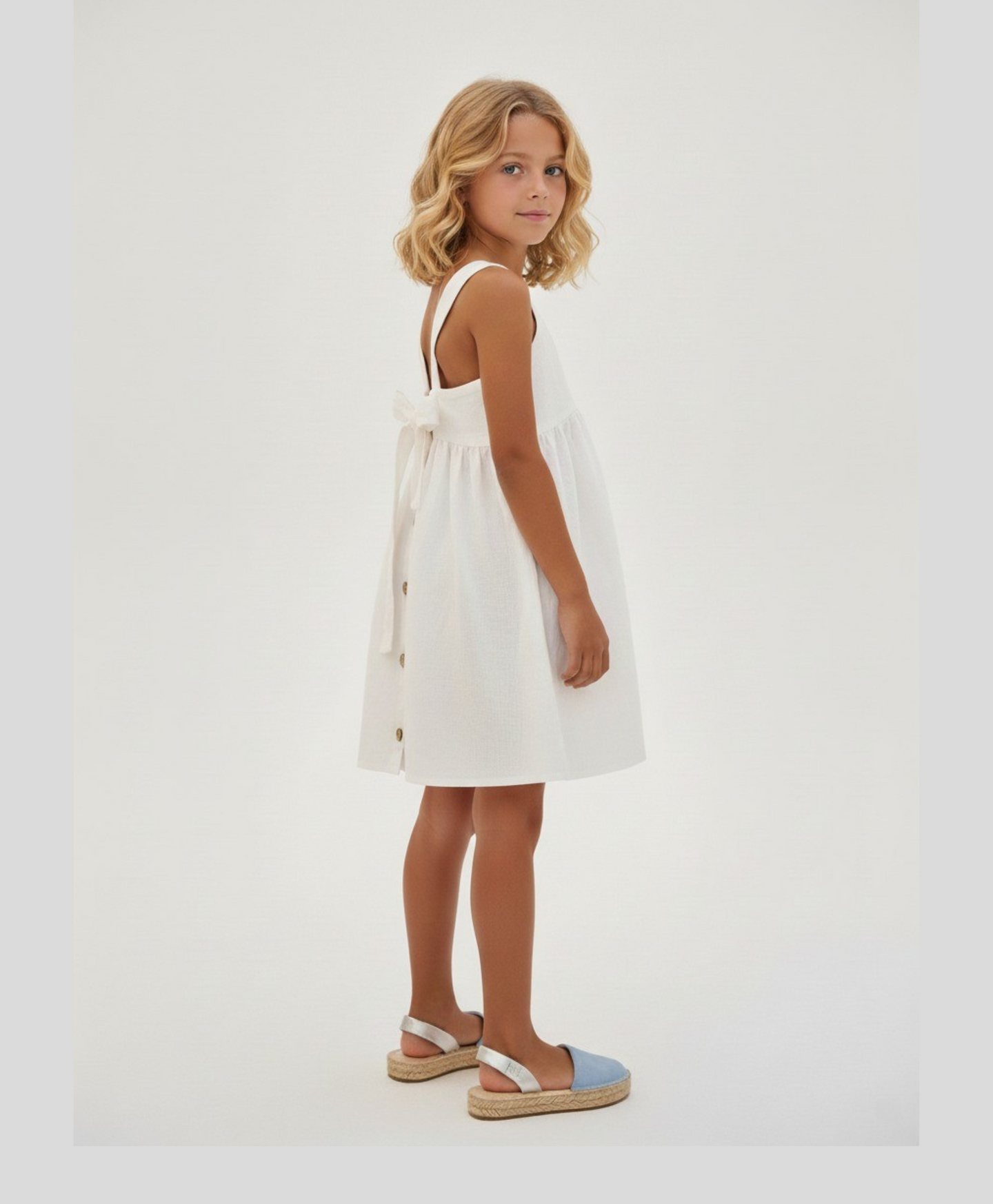 Young girl wearing a white dress with buttons on a plain background